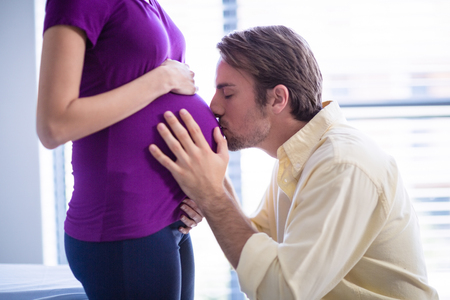 Man kissing pregnant womans belly in ward of hospitalの写真素材