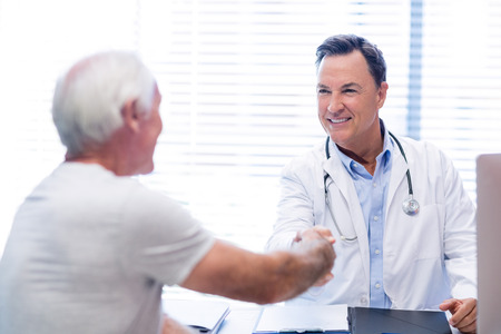 Doctor shaking hands with senior man in clinicの写真素材