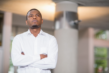 Thoughtful businessman with arms crossed standing at conference centreの写真素材