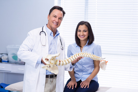 Portrait of physiotherapist and patient holding spine model in clinicの写真素材