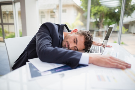 Tired businessman resting head on desk at conference centreの写真素材