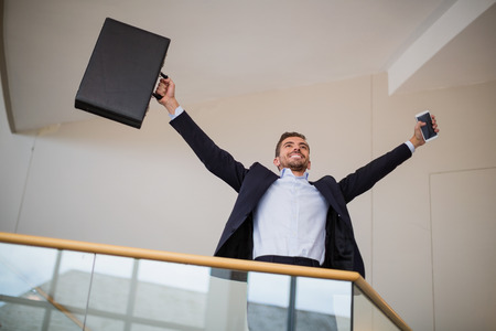 Happy businessman holding a briefcase and mobile phone cheeringの写真素材