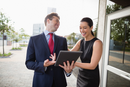 Businessman and colleague discussing over digital tablet and laughing outside the conference centreの写真素材