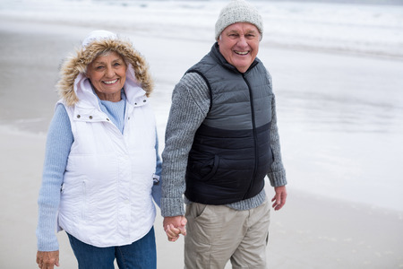 Senior couple walking toward the ocean while holding hands at beachの写真素材