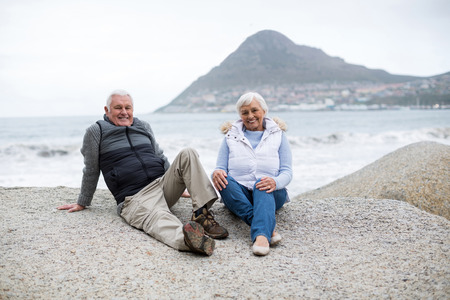 Portrait of happy senior couple sitting on rock at beachの写真素材