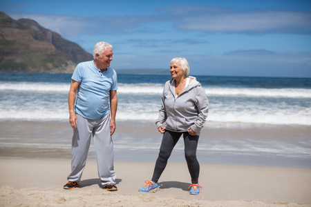 Happy senior couple doing stretching exercise on the beachの写真素材
