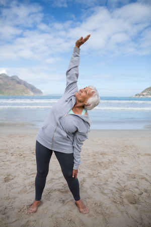 Happy senior woman doing stretching exercise on the beachの写真素材