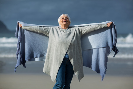 Portrait of smiling senior woman wrapped in shawl at beachの写真素材