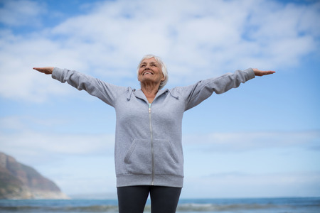 Happy senior woman doing stretching exercise on the beachの写真素材