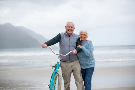 Portrait of senior couple standing with bicycle on the beachの写真素材