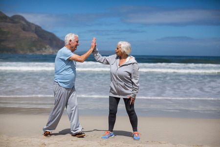 Happy senior couple giving high five after exercise on the beachの写真素材