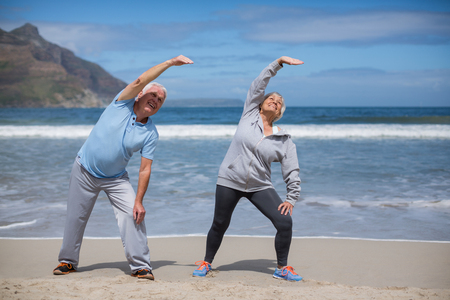 Happy senior couple doing stretching exercise on the beachの写真素材