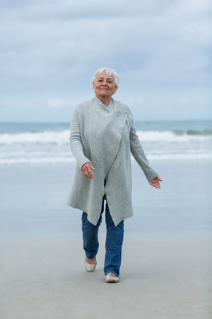Smiling senior woman walking on the beachの写真素材