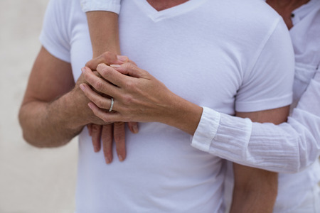 Mid section of couple standing with holding hands on the beachの写真素材