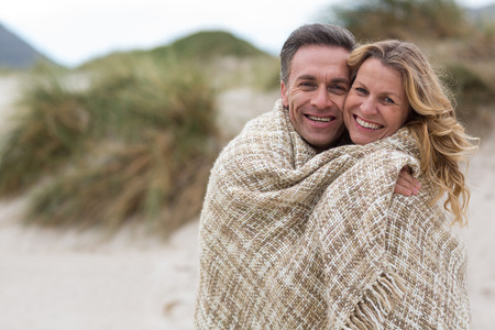 Portrait of mature couple wrapped in blanket on the beachの写真素材