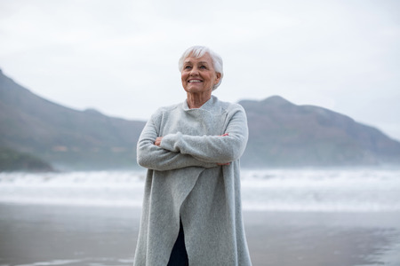 Smiling senior woman standing with arms crossed on the beachの写真素材