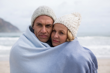 Romantic mature couple wrapped in blanket on the beachの写真素材