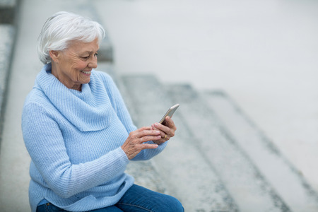 Senior woman sitting on the steps and using mobile phoneの写真素材