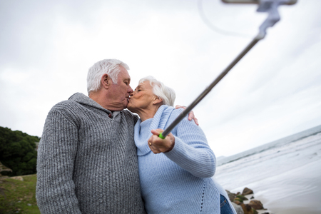 Senior couple taking a selfie from selfie stick on beachの写真素材