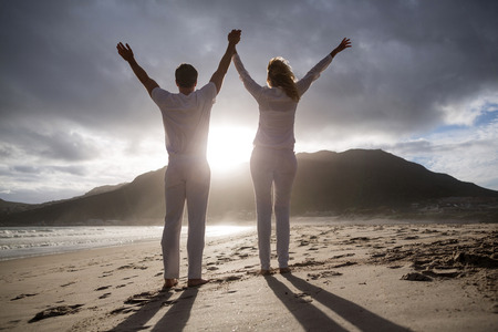 Rear view of couple standing with holding hands on the beachの写真素材