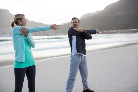 Mature couple doing stretching exercise on the beach