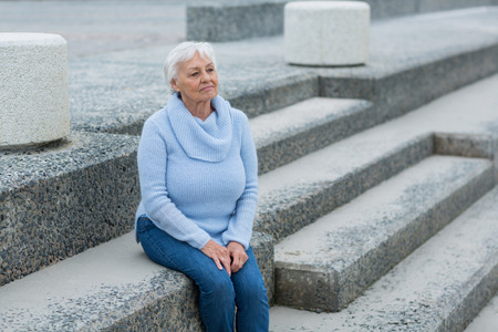 Thoughtful senior woman sitting on the steps near beachの写真素材