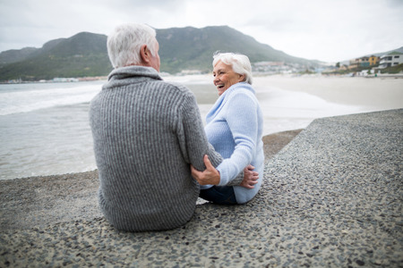 Happy senior couple sitting on rock at beachの写真素材