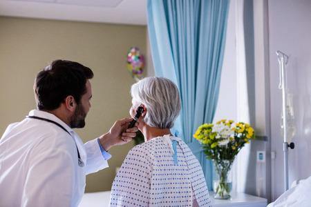 Doctor examining patients ear with otoscope in clinicの写真素材