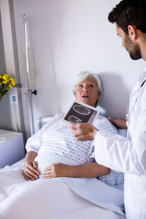 Male doctor discussing medical report over digital tablet with female senior patient in the ward at hospitalの写真素材