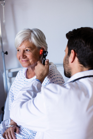 Doctor examining patients ear with otoscope in clinicの写真素材