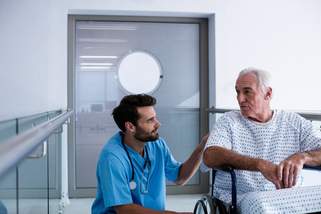 Doctor interacting with male senior patient on a wheelchair in the passageway
