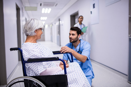 Male doctor interacting with senior patient on wheelchair in the corridorの写真素材
