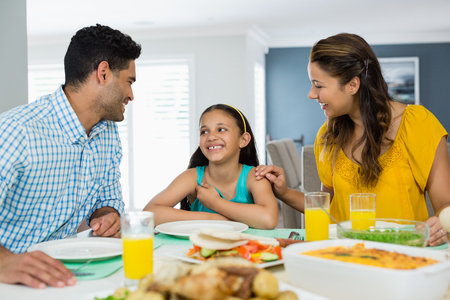 Daughter and parents interacting while having meal on table at homeの写真素材