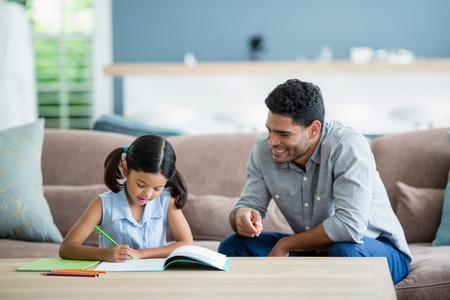 Father assisting her daughter in doing her homework at homeの写真素材