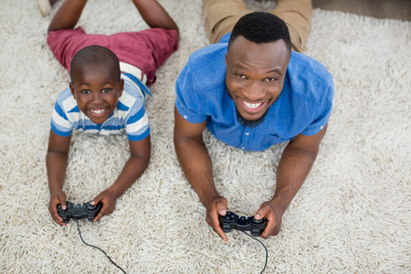 Portrait of father and son lying on rug and playing video game at homeの写真素材