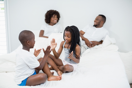 Kids having fun in bedroom while parents interacting in background at homeの写真素材
