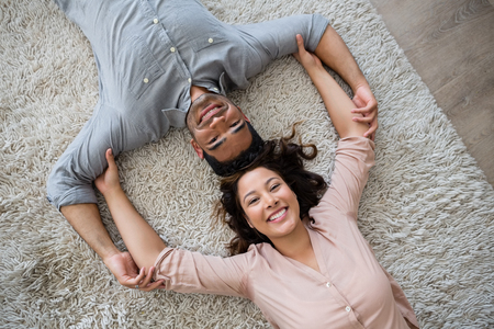 Portrait of happy couple lying on rug in living room at homeの写真素材