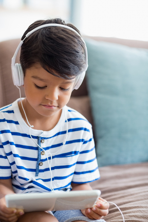 Boy listening music on digital tablet in living room at homeの写真素材