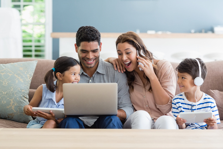 Parents and kids using laptop and digital tablet in living room at homeの写真素材