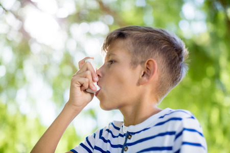Young boy using asthma inhaler in parkの写真素材