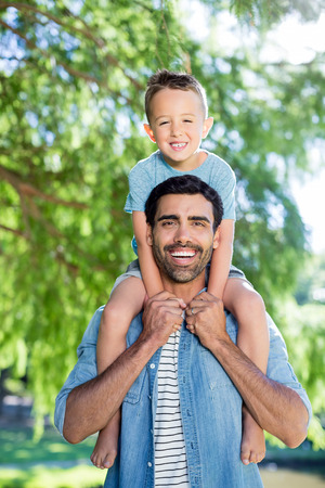 Father carrying son on his shoulders park in park on a sunny dayの写真素材