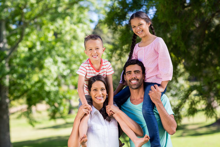 Portrait of parents carrying their children on shoulder in park on a sunny dayの写真素材