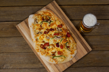 Overhead of delicious pizza served on pizza tray with a glass of beer on wooden plankの写真素材