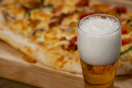 Delicious pizza served on pizza tray with a glass of beer on wooden plankの写真素材