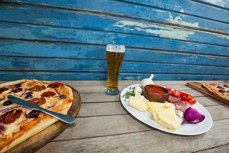 Delicious italian pizza served with glass of beer on wooden plankの写真素材