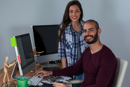 Photographer working at his desk with colleague in officeの写真素材