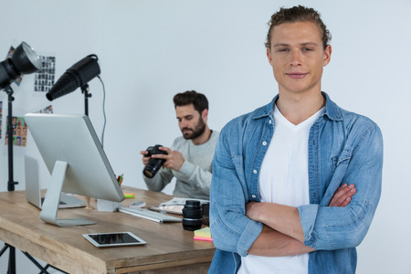 Portrait of smiling photographer standing with his arms crossed in studioの写真素材
