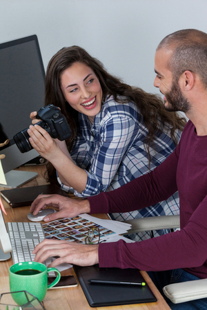 Photographer working at his desk with colleague in officeの写真素材