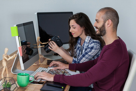 Photographer working at his desk with colleague in officeの写真素材