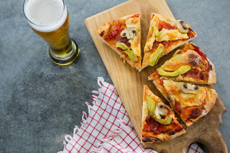 Pieces of italian pizza served with glass of beer on a chopping boardの写真素材